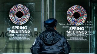 A security guard stands outside the building near signs advertising the International Monetary Fund/World Bank Spring Meetings in Washington, DC, on April 17, 2025.