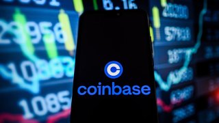 The Coinbase logo is displayed on a smartphone with stock market percentages on the background.