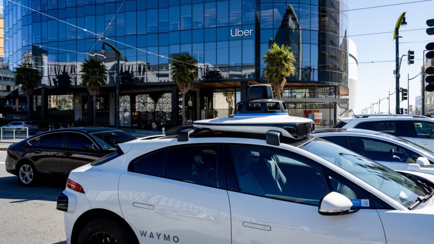 Self-driving Waymo vehicle driving past the headquarters of Uber, with signage visible, in the Mission Bay neighborhood, San Francisco, California, March 18, 2025.