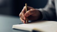 An individual meticulously jotting down notes in a notebook using an elegant pen, with a close-up on the writing hand.