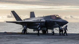 Crews walk towards a Royal Navy F-35B Lightning fighter jet to prepare it for take-off from the deck of British aircraft carrier HMS Prince Of Wales, in an undisclosed location, on April 24, 2025, following its deployment to the Indo-Pacific region.