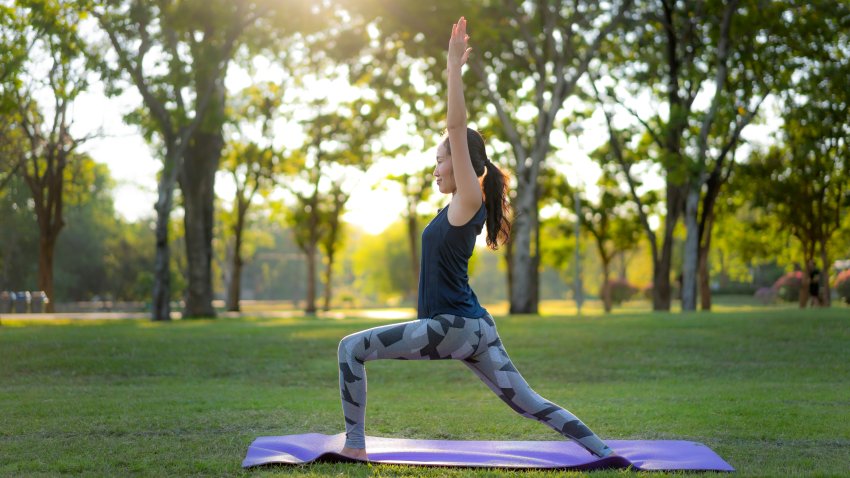 Young Asian woman practicing warrior 1 yoga in park at sunset.