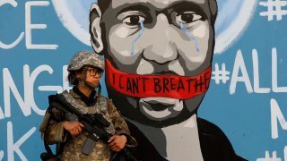 FILE — In this June 4, 2020 file photo a member of the California National Guard stands in front of a mural depicting George Floyd in Los Angeles.
