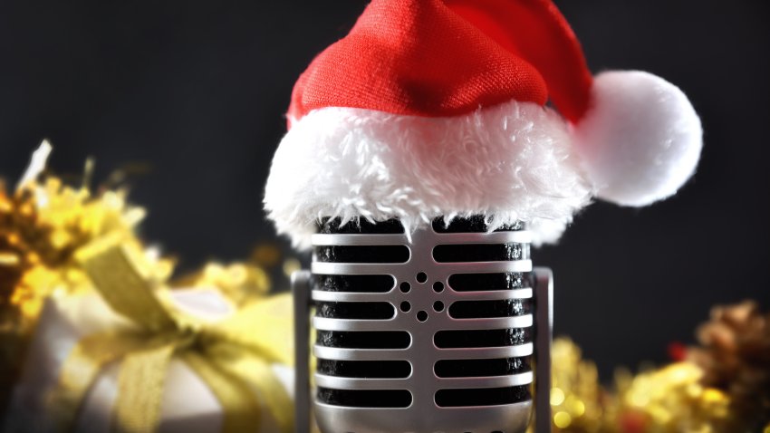Detail of retro microphone with Santa hat with gifts and golden Christmas decorations isolated on black background. Front view.