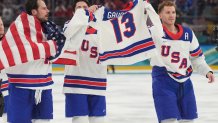 Feb 22, 2026; Milan, Italy; Auston Matthews (34) of the United States, Zach Werenski (8) of the United States and Matthew Tkachuk (19) of the United States hold up the jersey of John Gaudreau after defeating Canada in the men's ice hockey gold medal game during the Milano Cortina 2026 Olympic Winter Games at Milano Santagiulia Ice Hockey Arena. Mandatory Credit: Amber Searls-Imagn Images
