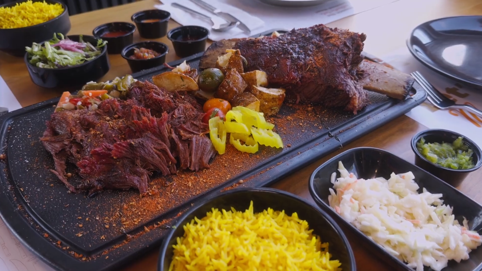 Elaborate BBQ platter with a large cut of meat, pulled pork, roasted potatoes, rice, and coleslaw.