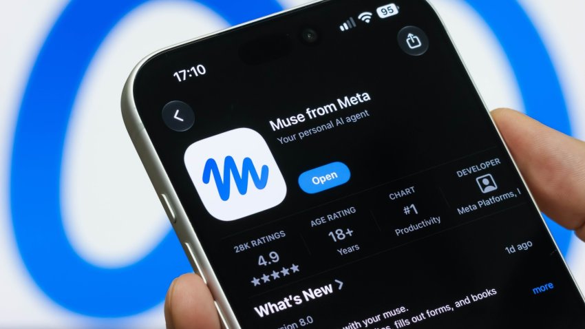 In this photo illustration, a hand holds a smartphone displaying the App Store listing for Meta's Muse AI assistant in front of the Meta logo on a computer screen.